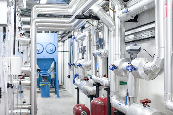 industrial room with metal pipes, valves, blue machinery, and red pressure tanks