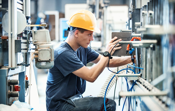 worker in a yellow hard hat operating machinery in an industrial setting with cables and control panels