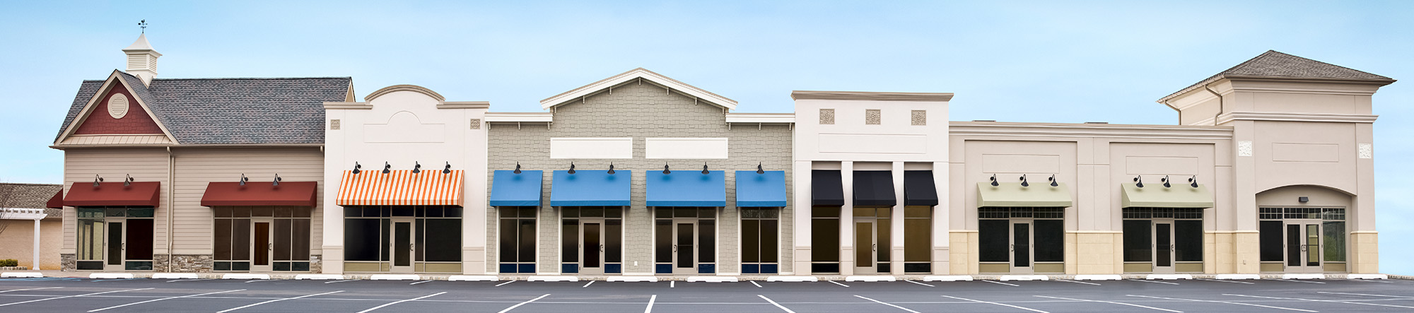 empty strip mall storefronts with colored awnings under blue sky