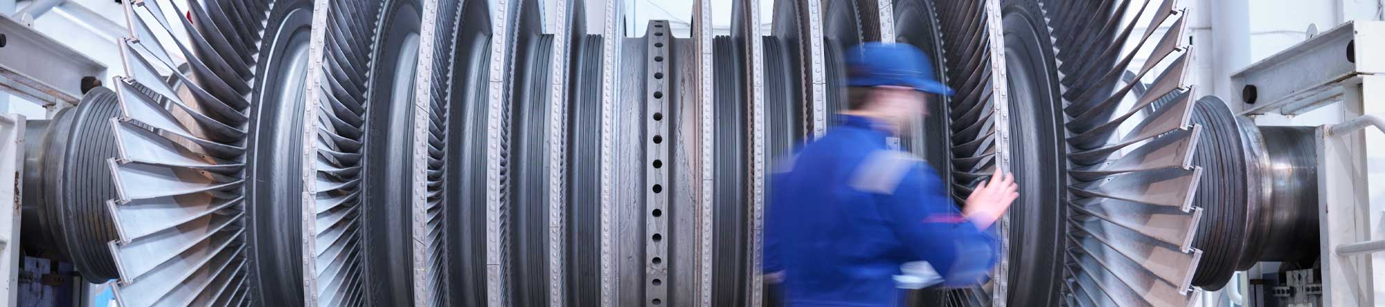 worker in blue uniform inspecting a large industrial turbine with multiple blades
