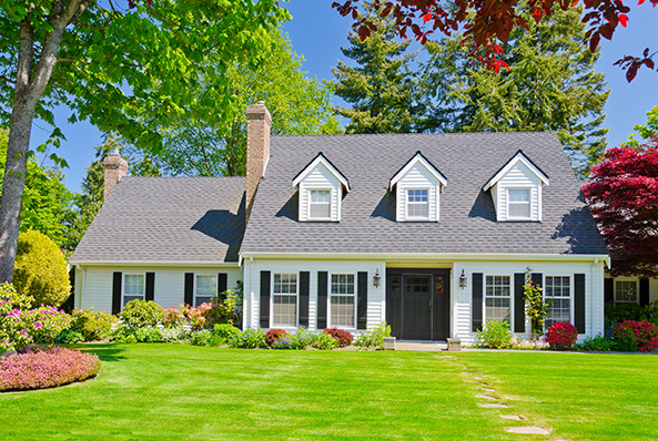 suburban house with white siding, black shutters, dormer windows, and a landscaped front yard