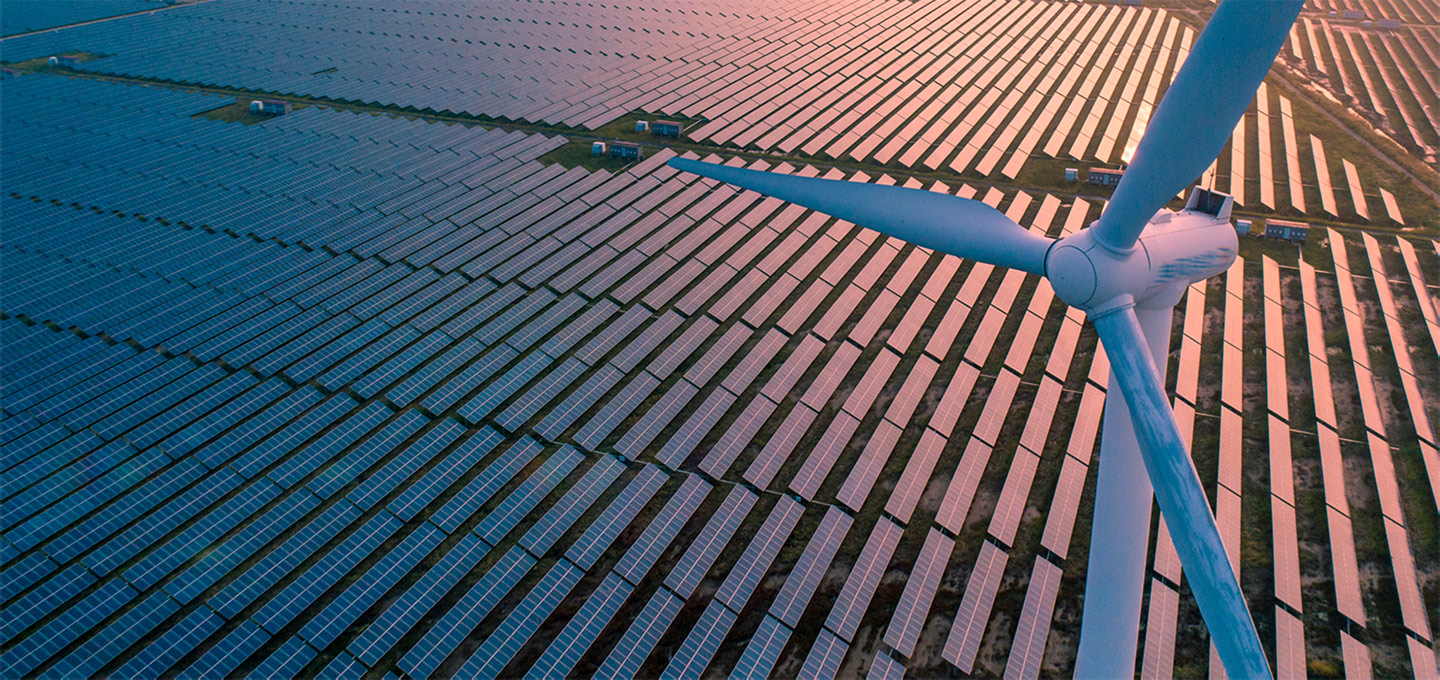 Aerial view of a renewable energy farm featuring rows of solar panels and wind turbines at sunset.
