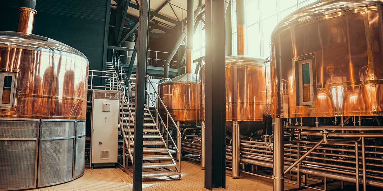 craft brewery interior featuring large copper brewing tanks, fermentation vessels, stainless steel piping, and industrial brewery equipment