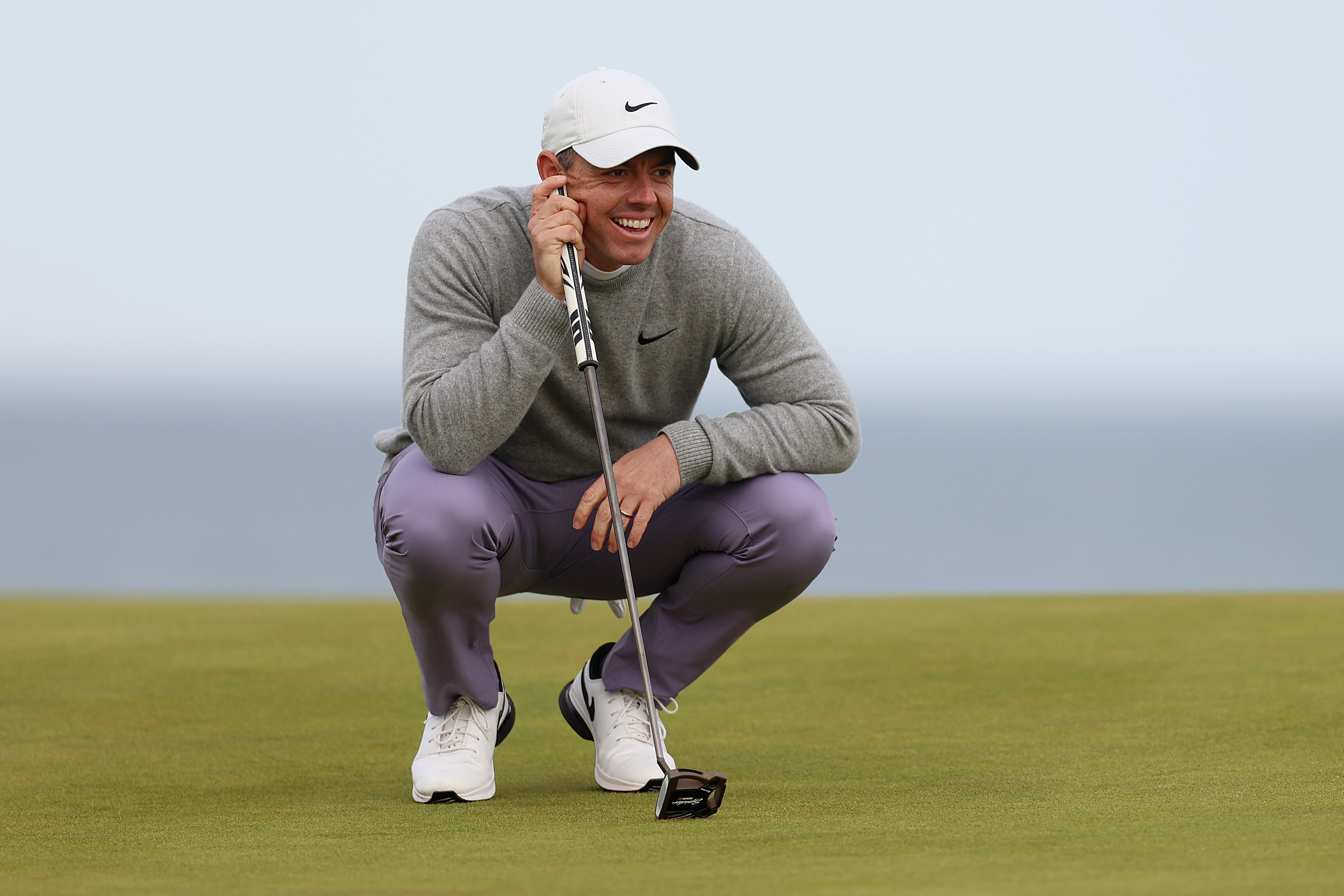 Rory McIlroy preparing to putt, strategic approach in golf, outdoor sports activity, golf as a wellness activity, FM mission of promoting health, golf attire and equipment, coastal golf course scene, enhancing concentration through sports, strategic thinking in golfing, benefits of golfing for mental health